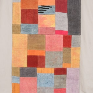 May include: A patchwork quilt with squares of various colors, including orange, red, pink, gray, and blue. The quilt is made of different fabrics and textures, creating a unique and interesting design.