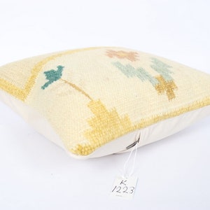 May include: Cream-coloured square cushion with a floral design in shades of yellow, teal, and peach. The cushion has a textured surface and a white backing. A tag with the number 1223 is attached.