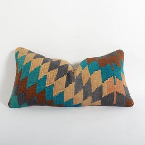 May include: Rectangular pillow with a geometric pattern in shades of teal, brown, gray, and tan. The pillow has a woven texture and is designed for decorative use. The pillow's dimensions are not visible in the image.