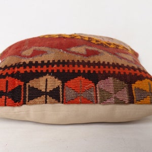 May include: A colorful throw pillow with a geometric pattern in shades of red, orange, brown, and beige. The pillow has a white fabric backing.