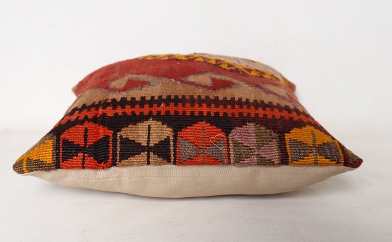 May include: A colorful throw pillow with a geometric pattern in shades of red, orange, brown, and beige. The pillow has a white fabric backing.
