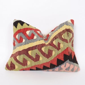 May include: A colorful, patterned pillow with a geometric design in shades of red, green, yellow, blue, and black. The pillow is made of woven fabric and has a traditional Turkish kilim style.