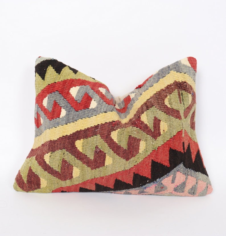 May include: A colorful, patterned pillow with a geometric design in shades of red, green, yellow, blue, and black. The pillow is made of woven fabric and has a traditional Turkish kilim style.