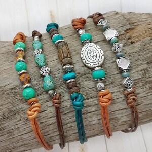 May include: Five leather bracelets with turquoise and silver beads. The bracelets have different charms, including a silver turtle, a silver square, and a wooden bead.