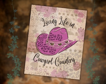 Può includere: Un cappello da cowboy rosa con un motivo a stampa leopardata e una fascia marrone. Il cappello è su uno sfondo con stelle, cuori e fiori. Il testo "Loving Life in Cowgirl Country" è scritto sotto il cappello.