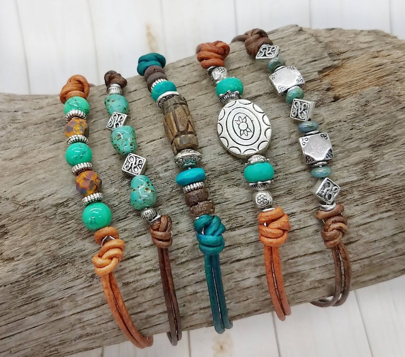 May include: Five leather bracelets with turquoise and silver beads. The bracelets have different charms, including a silver turtle, a silver square, and a wooden bead.