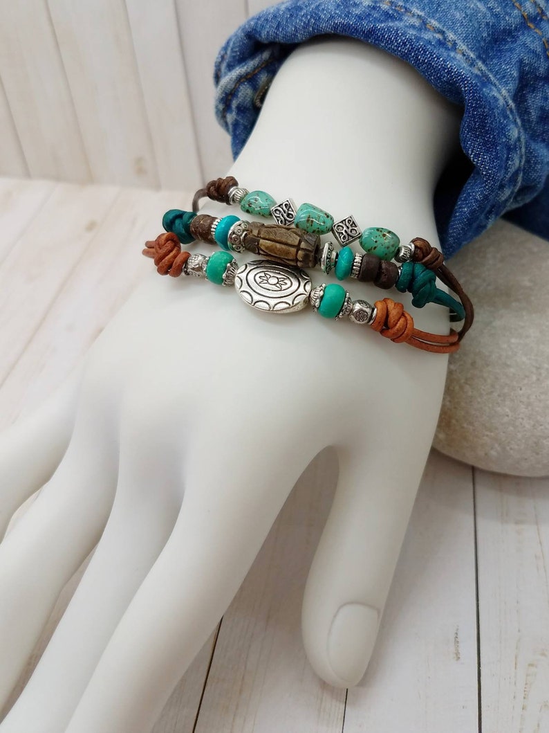 May include: A set of three leather bracelets with turquoise and brown beads, a silver charm, and a wooden bead.