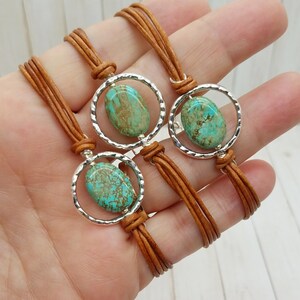 May include: Three leather bracelets with turquoise stones set in silver circles. The bracelets are brown and have a braided design.