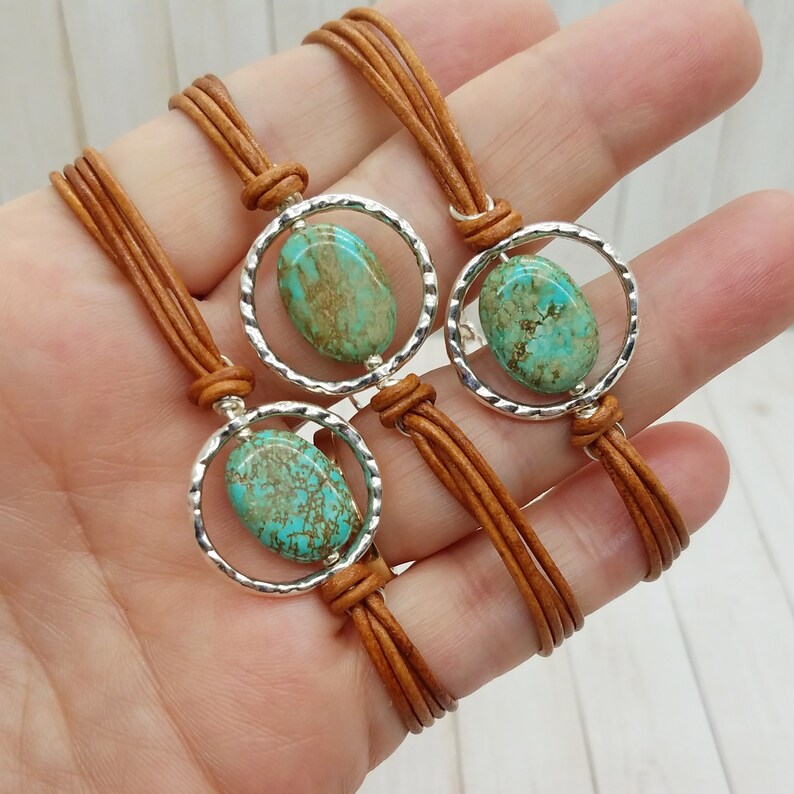 May include: Three leather bracelets with turquoise stones set in silver circles. The bracelets are brown and have a braided design.