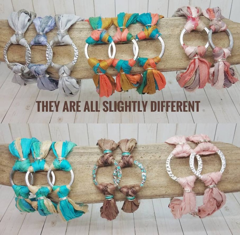 K&ouml;nnte beinhalten: Sechs Armb&auml;nder mit silbernen Ringen und bunten Stoffquasten. Die Armb&auml;nder sind aus verschiedenen Stoffen gefertigt, darunter T&uuml;rkis, Braun, Rosa und Grau. Der Text "THEY ARE ALL SLIGHTLY DIFFERENT" ist unter den Armb&auml;ndern gedruckt.