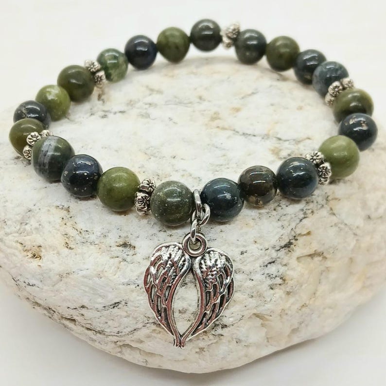 Puede incluir: Una pulsera de cuentas con cuentas de piedras preciosas de color verde oliva y verde azulado oscuro. La pulsera tiene un dije plateado en forma de alas de &aacute;ngel. Las cuentas est&aacute;n ensartadas en un cord&oacute;n el&aacute;stico y est&aacute;n acentuadas con espaciadores plateados.