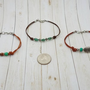 May include: Three leather bracelets with silver clasps and green beads. The center bracelet has a silver charm with a design.
