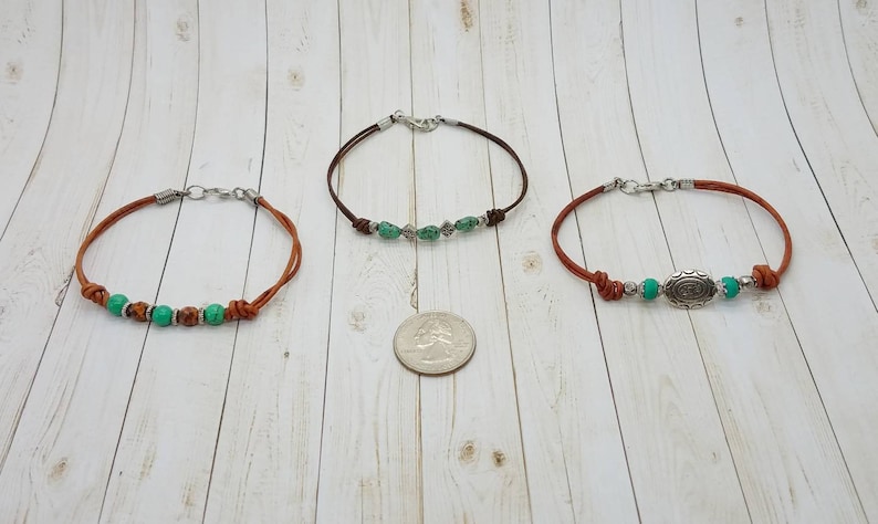 May include: Three leather bracelets with silver clasps and green beads. The center bracelet has a silver charm with a design.