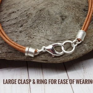 May include: A brown leather cord bracelet with a large silver clasp and ring for ease of wearing.