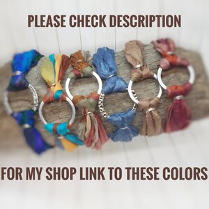 K&ouml;nnte beinhalten: Nahaufnahme von sieben bunten Seidenbandarmb&auml;ndern mit silbernen Ringen. Die Armb&auml;nder sind auf einer Holzoberfl&auml;che angeordnet.  "PLEASE CHECK DESCRIPTION FOR MY SHOP LINK TO THESE COLORS" steht in brauner Schrift unter den Armb&auml;ndern.