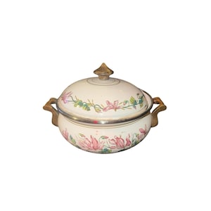 May include: Cream-colored enamelware casserole dish with a lid, featuring floral designs in pink and green. The dish has a silver rim, wooden handles, and a gold-colored finial on the lid. A vintage kitchenware item.