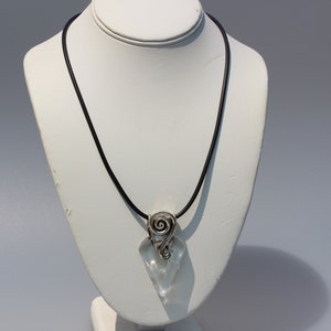 May include: A silver pendant necklace with a clear quartz crystal and a spiral design. The necklace is on a black cord.
