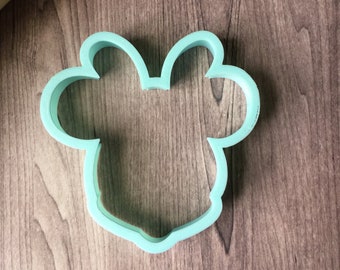 May include: A light blue plastic cookie cutter shaped like a cartoon mouse head.