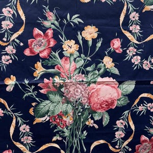May include: A navy blue floral fabric featuring a bouquet of pink and red roses, small pink flowers, and yellow blossoms. The design includes gold ribbons and green leaves. The fabric is likely for sewing or crafting.