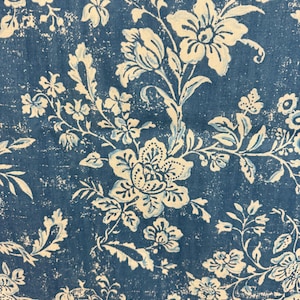 May include: Close-up of a blue fabric with a distressed floral pattern. The design features large, stylized flowers and foliage in off-white and light blue, creating a vintage aesthetic. The background is a deep blue with a textured, worn appearance.