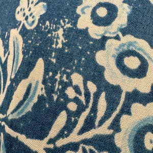 May include: Close-up of a blue and white floral pattern on fabric. The design features stylized flowers and leaves in shades of blue and white against a textured blue background. The fabric appears to be cotton or a similar material.