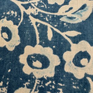 May include: Close-up of a fabric with a repeating floral pattern. The design features white flowers and leaves against a deep blue background. The fabric has a textured appearance, with visible weave details.
