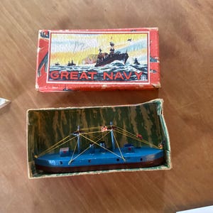 May include: Vintage toy boat in a box. The blue boat has a red hull and yellow rigging. The box is red with the words "GREAT NAVY" and an illustration of a ship at sea.