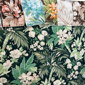 May include: A close-up of a dark green fabric with a white floral pattern. The fabric features large white flowers and green leaves, creating a tropical feel.