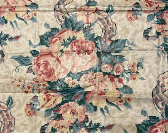May include: A beige fabric with a floral pattern featuring pink, red, and yellow flowers with green leaves. The flowers are arranged in a repeating pattern and are connected by a ribbon-like design.