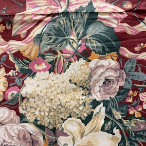 May include: A red fabric with a floral pattern featuring white, pink, and yellow flowers, green leaves, and a pink ribbon.