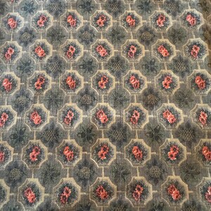 May include: Close-up of a fabric with a repeating pattern of pink flowers within octagonal shapes. The flowers are surrounded by a dark blue and beige background, creating a vintage aesthetic. The fabric has a textured appearance.