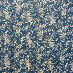 May include: A blue fabric with a white floral pattern. The design features detailed flowers and leaves, creating a vintage or antique aesthetic. The fabric has a slightly distressed look, adding to its charm.