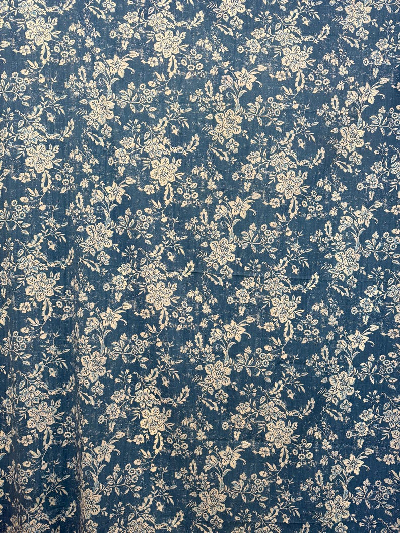 May include: A blue fabric with a white floral pattern. The design features detailed flowers and leaves, creating a vintage or antique aesthetic. The fabric has a slightly distressed look, adding to its charm.