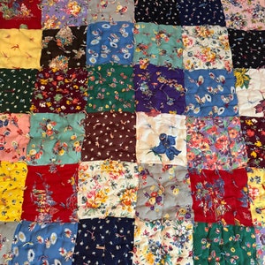 May include: A patchwork quilt with a variety of floral patterns in shades of blue, green, red, yellow, and purple. The quilt is made up of squares of different fabrics, each with a unique design.