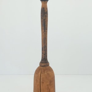 May include: A vintage wooden muddler with a rounded top and a long, textured handle. The muddler has a bulbous base and is made of light brown wood with darker, aged accents. It is a kitchen tool.
