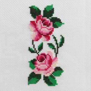 May include: Cross-stitch embroidery of two pink roses with green leaves on a white background.