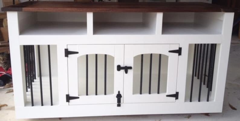 May include: White wooden dog crate with two doors and a top shelf. The crate has black metal bars and black metal hinges. The doors have a black metal latch.