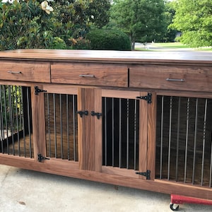 May include: A wooden dog crate with three drawers and two doors. The crate is made of walnut wood and has black metal bars on the doors. The crate is sitting on a concrete surface.