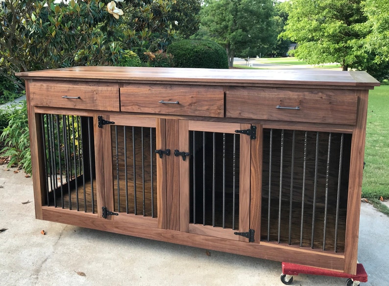 May include: A wooden dog crate with three drawers and two doors. The crate is made of walnut wood and has black metal bars on the doors. The crate is sitting on a concrete surface.