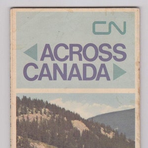 May include: A vintage CN Rail travel poster featuring a train traveling through a mountainous landscape. The poster has a blue and purple background with the text "CN ACROSS CANADA" in white.