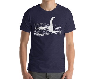 May include: A navy blue t-shirt with a white silhouette of the Loch Ness Monster on a wavy water background.