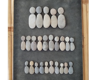 May include: A black framed artwork featuring a design of people made from small, smooth stones. The artwork is arranged in three rows, with the top row having five people, the middle row having 18 people, and the bottom row having 18 people.