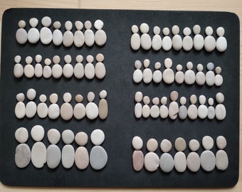 May include: A black background with rows of small, white, gray, and brown stones arranged in the shape of people.