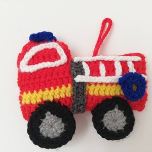 May include: A red, white, and blue crocheted fire truck ornament with a yellow stripe and black wheels.
