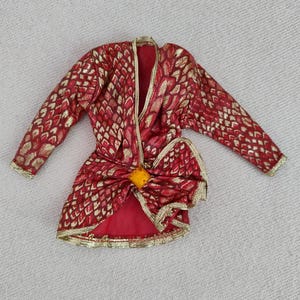 Könnte beinhalten: Eine rot-goldene gemusterte Jacke mit einer großen Schleife in der Taille. Die Jacke hat lange Ärmel und einen V-Ausschnitt.