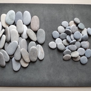 May include: Two groups of smooth, gray and brown stones on a gray surface. The stones are various sizes and shapes.