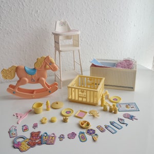 May include: A set of pink and yellow plastic baby toys, including a rocking horse, a cot, a high chair, and various accessories. The toys are arranged on a white surface.