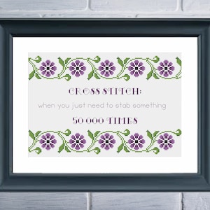 May include: Framed cross-stitch art with a navy blue frame. The artwork features the text "CROSS STITCH: when you just need to stab something 50 000 TIMES" in a cross-stitch font. Floral border with purple flowers and green leaves.
