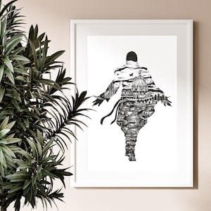 May include: Black and white art print in a white frame. The artwork depicts a figure with outstretched arms, filled with a detailed cityscape. The print is set against a neutral wall, with a leafy green plant in the foreground.