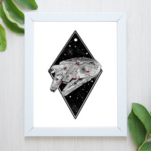 May include: White framed art print featuring a detailed illustration of the Millennium Falcon starship. The ship is set against a black diamond shape filled with stars. The artwork is in black, white, and red.